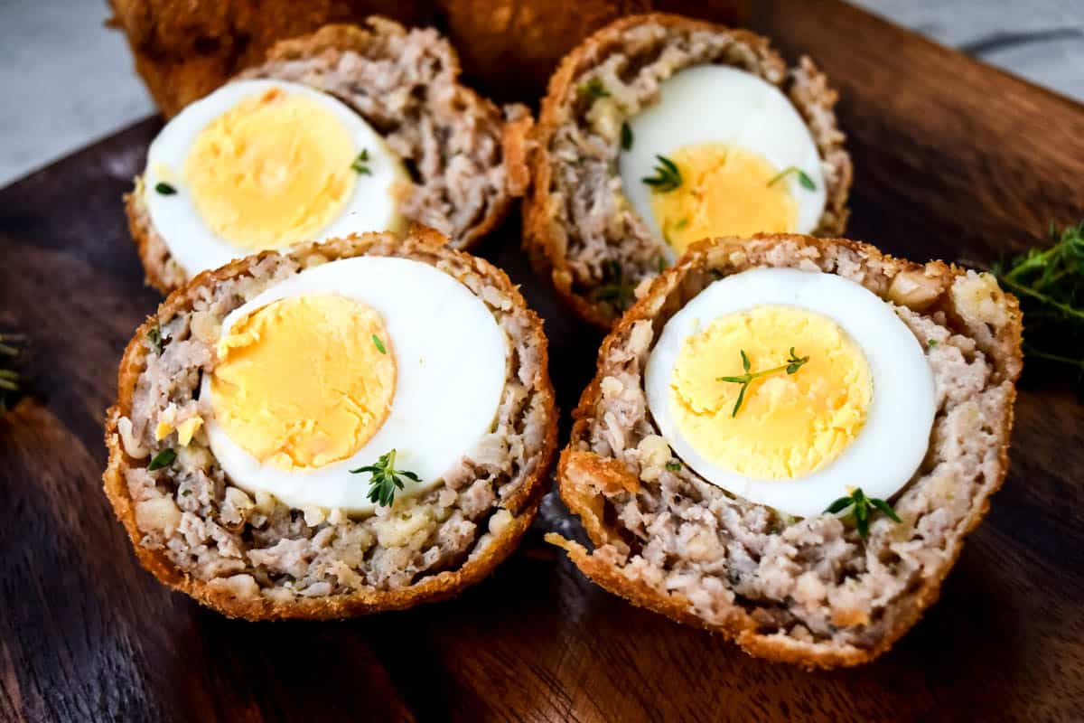 A wooden plate with two Scotch eggs both cut in half.