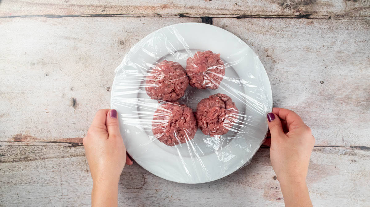 Two hands are holding a plate of four turkey mince balls covered in clingfilm.