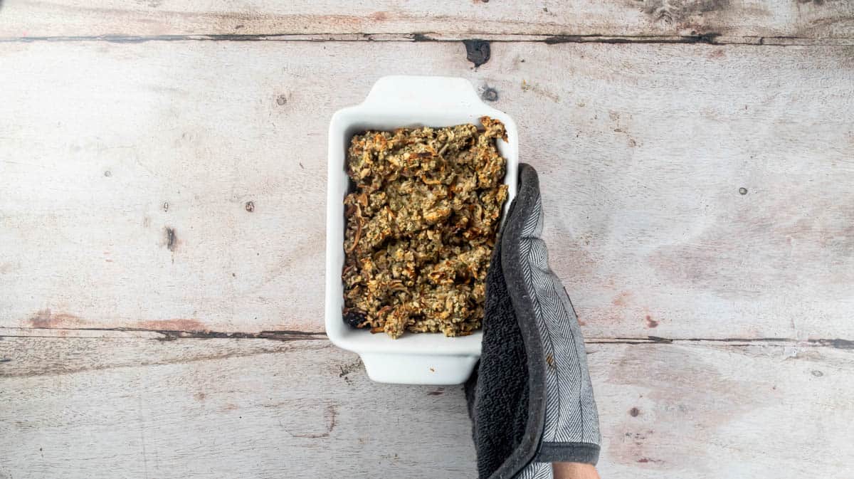 A gloved hand is holding a baking dish filled with cooked stuffing.