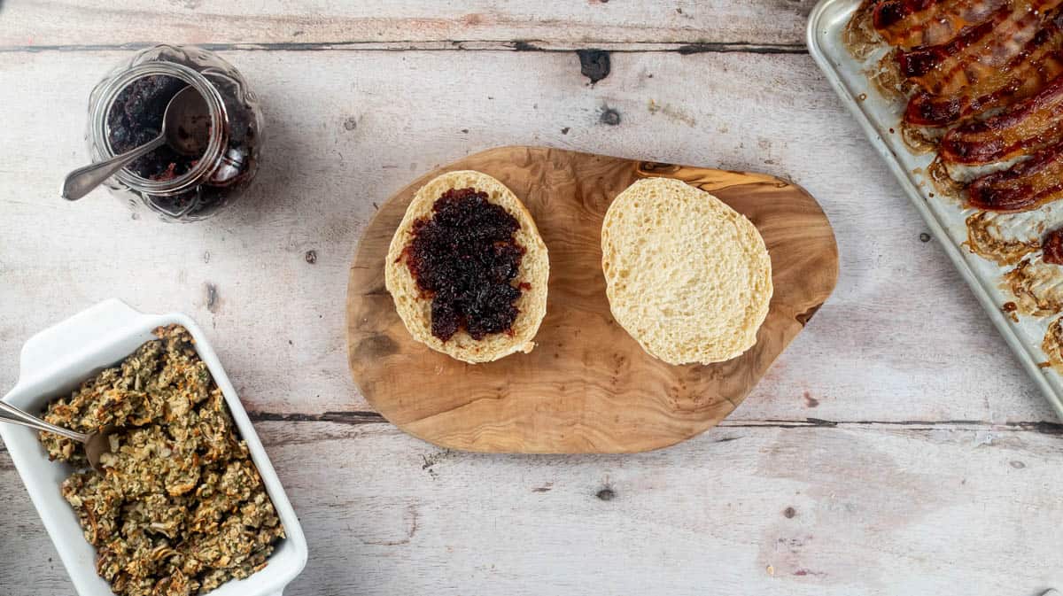 A sliced burger buns that has been toasted and spread on one side with cranberry sauce.