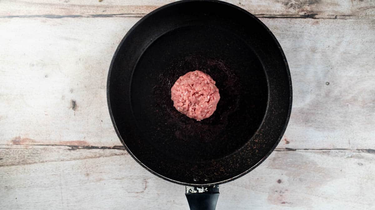 An overhead view of a black frying pan with a turkey mince ball sat in the middle.