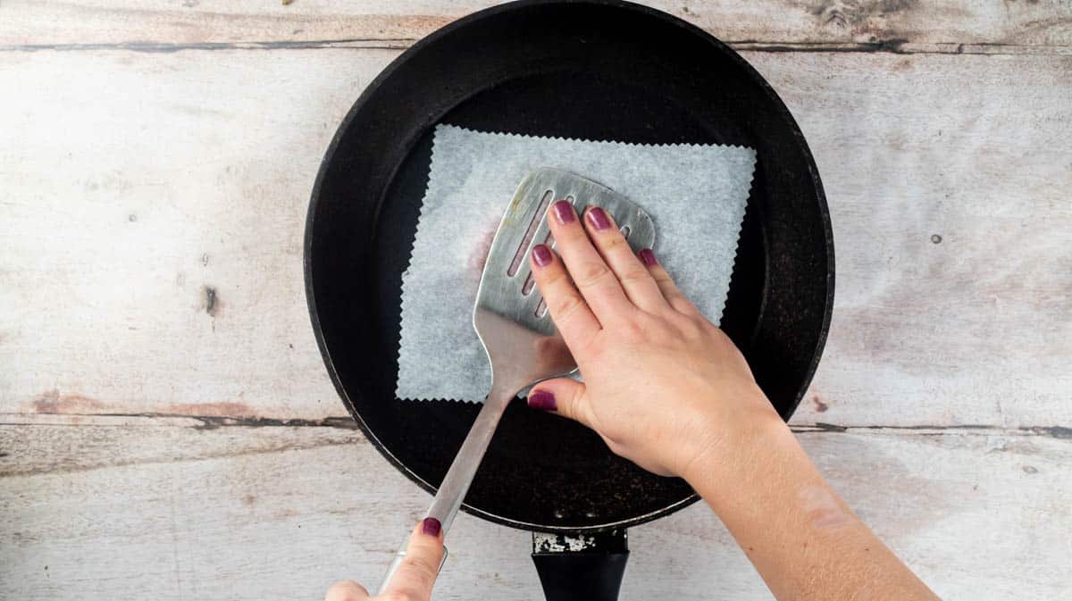 The turkey mince ball is covered with a square of baking paper and a hand is using a metal spatula to press down on the top to form the smashed burger.