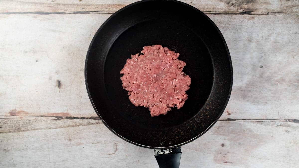 The smashed burger in the middle of a black frying pan.