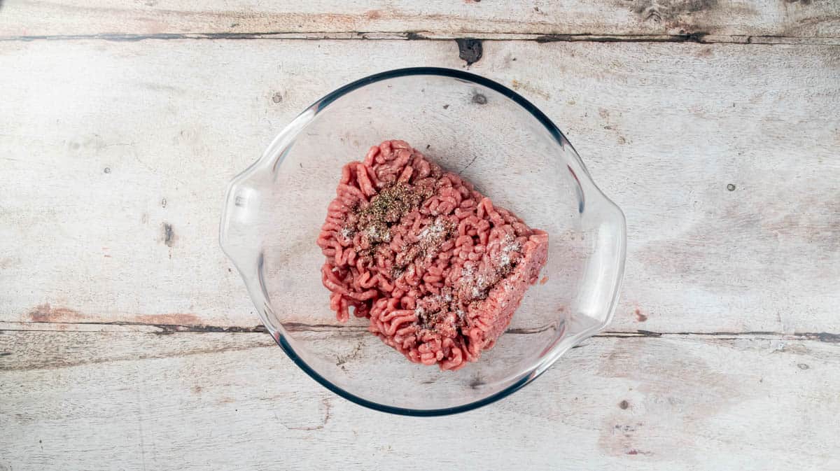 An overhead view of a glass bowl containing turkey mince and seasoning.