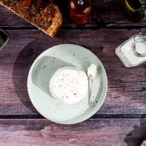An overhead view of drained Ricotta on a plate with a small spoon next to it. The plate is surrounded by decorative items.
