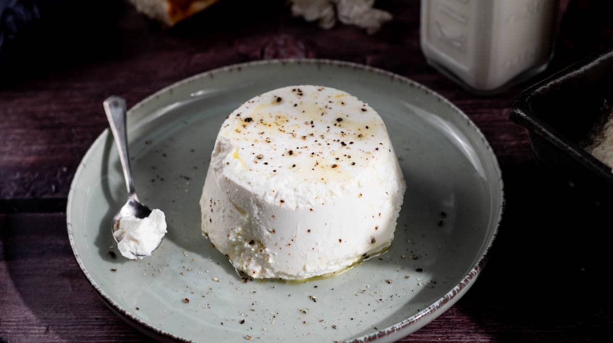 A close up front view of ricotta with a spoon next to it, both on a green plate.