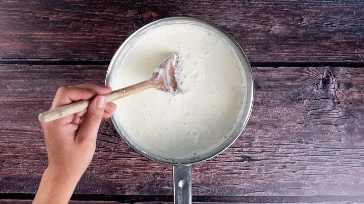 A hand is gently stirring the milk to incorporate the vinegar.